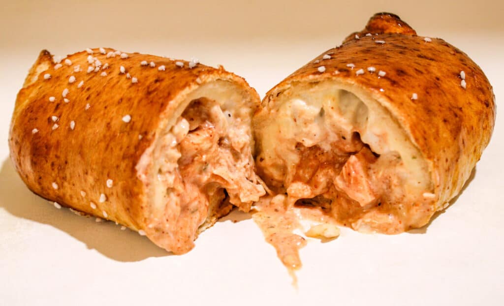 Cross-section of a golden puff pastry roll filled with creamy, sausage-cheese filling, with filling oozing out onto a white plate.